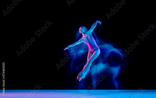 Flying bird. Young and graceful ballet dancer on black studio background in neon mixed light. Art, motion, action, flexibility, inspiration concept. Flexible caucasian ballet dancer, weightless jumps.