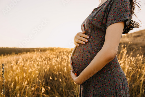 Closeup of a pregnant woman in a field with dry grass, holding hands on her belly. photo