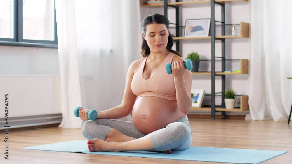sport, fitness and pregnancy concept - happy pregnant woman with light dumbbells exercising at home sport, fitness and pregnancy concept - happy pregnant woman with light dumbbells exercising at home
