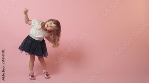 A cute little girl jumping, laughing and indulging. Beautiful bright festive outfit. Pink background.