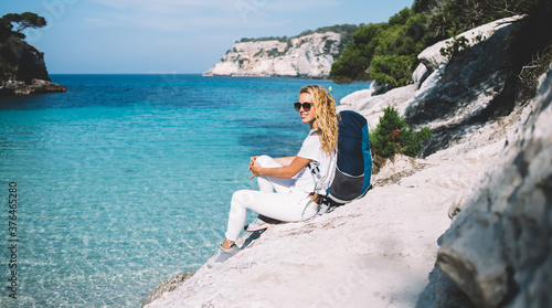 Carefree Caucasian female backpacker in stylish sunglasses enjoying travel adventure for exploring Spanish nature environment on breathtaking Menorca located on coastline of Balearic islands