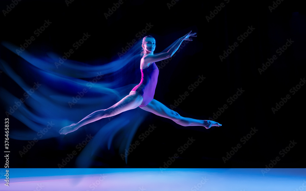 Flying bird. Young and graceful ballet dancer on black studio background in neon mixed light. Art, motion, action, flexibility, inspiration concept. Flexible caucasian ballet dancer, weightless jumps.