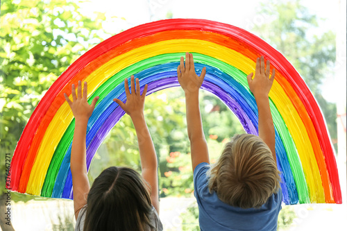 Children touching picture of rainbow on window. Stay at home concept