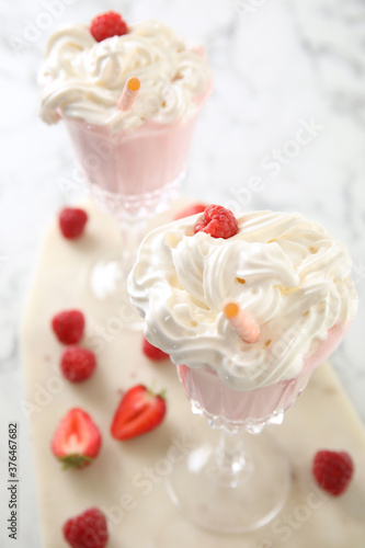 Tasty milk shake with whipped cream and fresh berries on light table, closeup