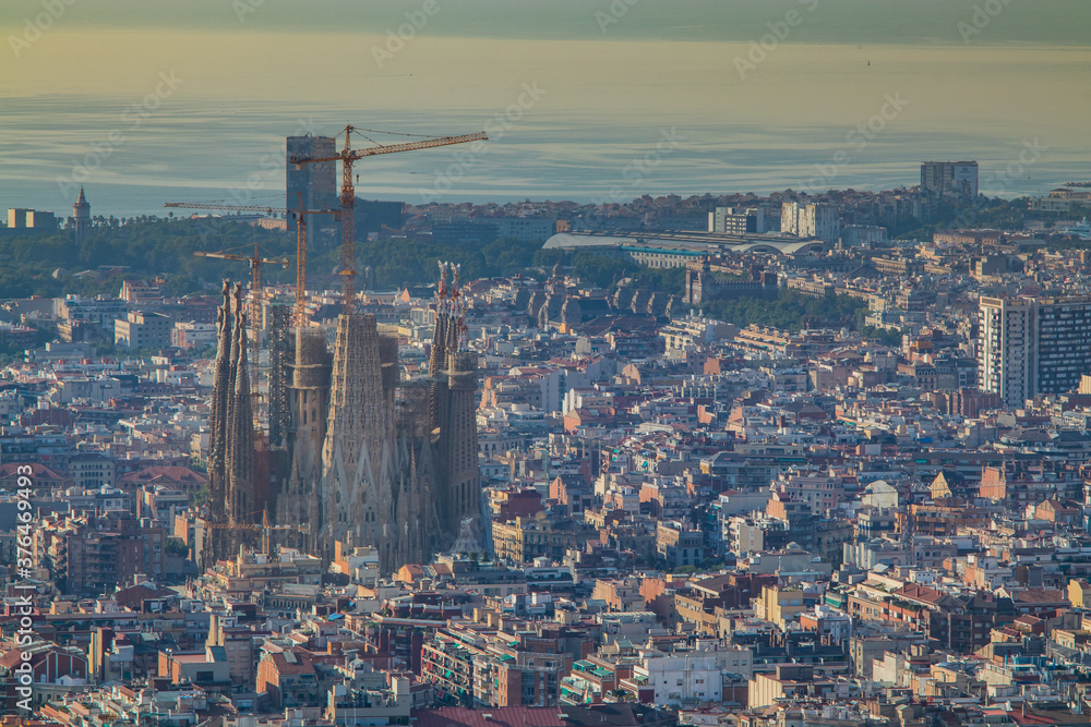 Picture of Sagrada Familia, church in Barcelona, surrounded by multitude of other buildings on a sunny summer morning.