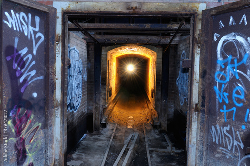 Single light in the tunnel of an abandoned brick factory with graffiti
