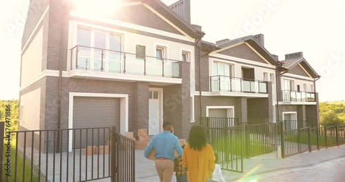 Rear of African American family with small children walking and moving in new home at suburb. Mother and father carrying boxes at house and little kids helping. Parents, son and daughter settling in.