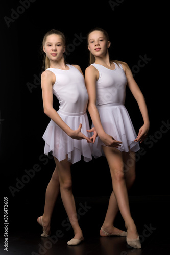 Two cute girls gymnasts in beautiful swimsuits perform exercises on a black background.