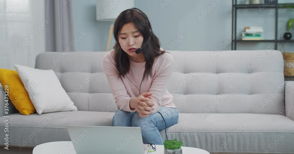 Beautiful young woman sitting on sofa and using laptop computer to work. Smart Asian female customer support worker consulting, talking to clients via video chat conference. Business, service. Beautiful young woman sitting on sofa and using laptop computer to work. Smart Asian female customer support worker consulting, talking to clients via video chat conference. Business, service.