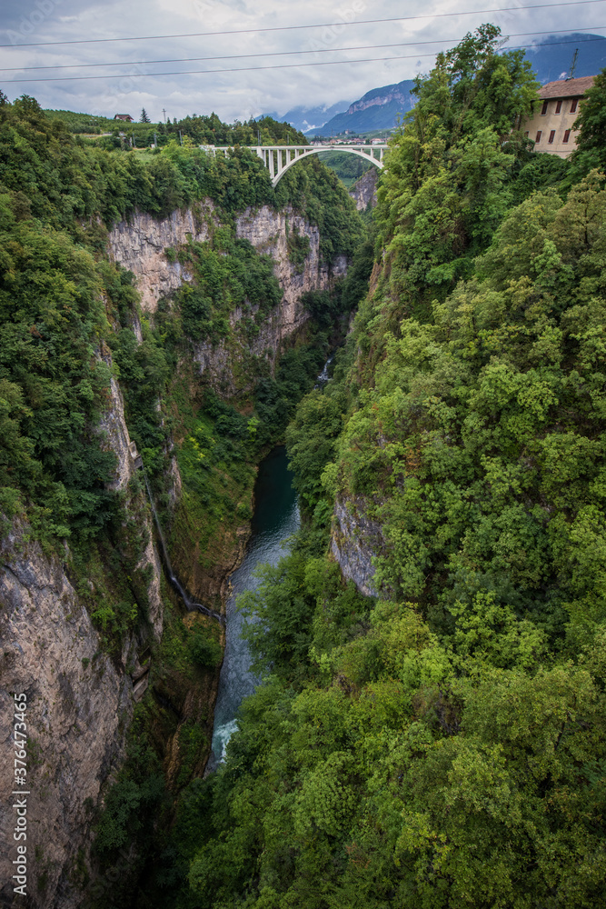 Deep gorge valley with river of Adige in the bottom behind the dam of lake Giustina in Italy, close to the city of Cles. White train bridge visible in the background.