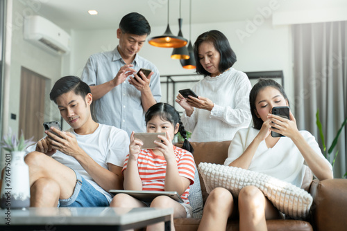 5G Technology for Families concept.Everyone sitting in sofa and using digital devices in living room.Big family grandmother grandfather and kids spending time together at home.