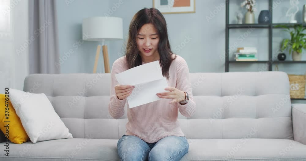 Pretty smiling Asian girl sitting on sofa and opening submission letter from university/college. Excited young woman reading response message and being happy. Education, study. Pretty smiling Asian girl sitting on sofa and opening submission letter from university/college. Excited young woman reading response message and being happy. Education, study.
