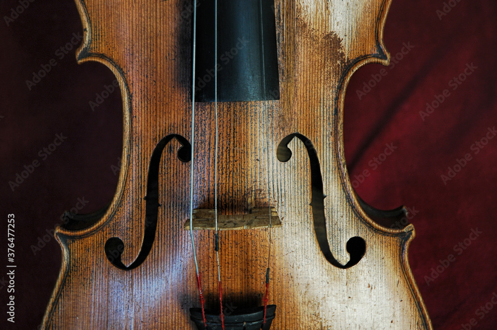 Beautifully designed old violin with missing strings set against a burgundy red velvet background, cropped frontal view of the classic wooden string instrument used in a variety of musical genres Beautifully designed old violin with missing strings set against a burgundy red velvet background, cropped frontal view of the classic wooden string instrument used in a variety of musical genres