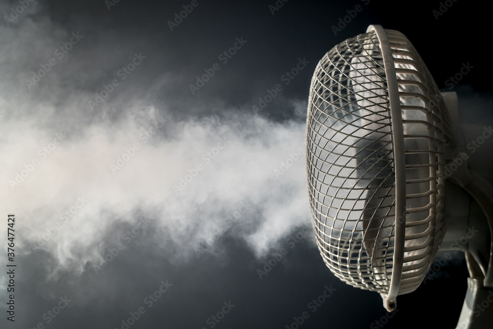 Detail view of a white electric desktop fan on a black background and reflective floor with visible fog or mist blowing through. Concept of freshness with a fan - obrazy, fototapety, plakaty 