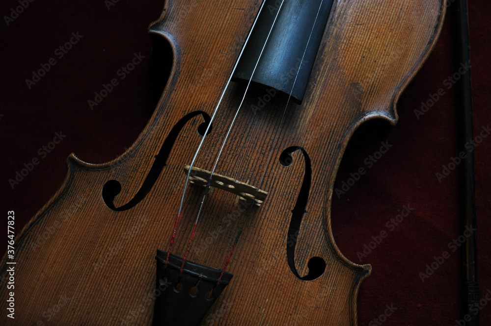 Beautifully designed old violin with missing strings set against a burgundy red velvet background, cropped frontal view of the classic wooden string instrument used in a variety of musical genres Beautifully designed old violin with missing strings set against a burgundy red velvet background, cropped frontal view of the classic wooden string instrument used in a variety of musical genres
