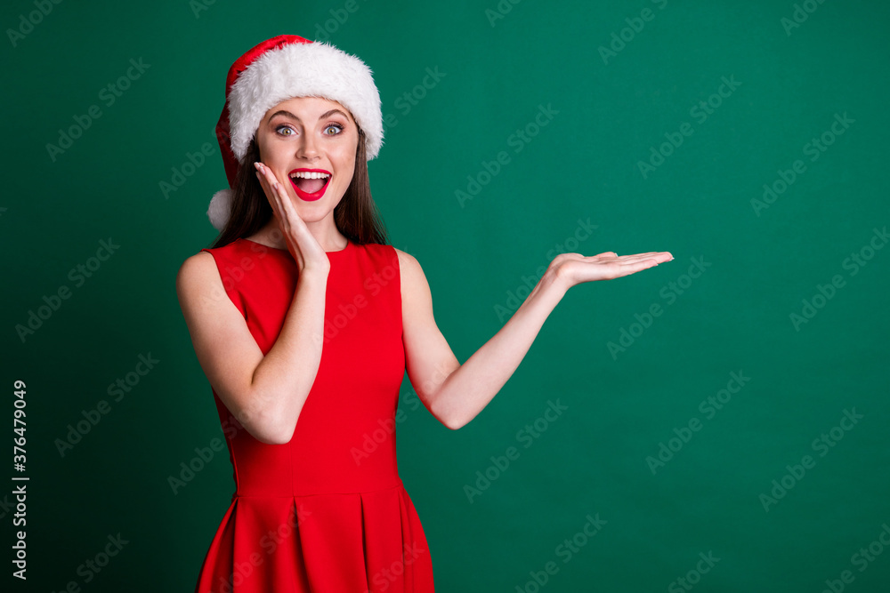 Photo of charming funny shocked lady hold open arm palm newyear sale discount decor product addicted shopper wear x-mas snow girl costume dress santa cap isolated green color background Photo of charming funny shocked lady hold open arm palm newyear sale discount decor product addicted shopper wear x-mas snow girl costume dress santa cap isolated green color background