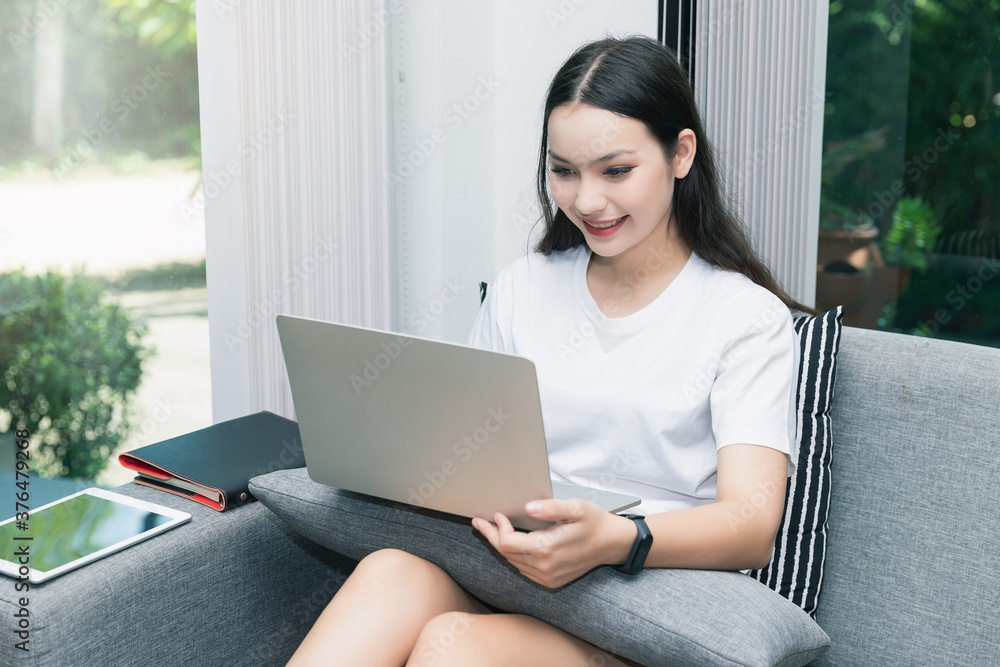 Pretty smiling young woman sitting on sofa and working on laptop. Pretty smiling young woman sitting on sofa and working on laptop.