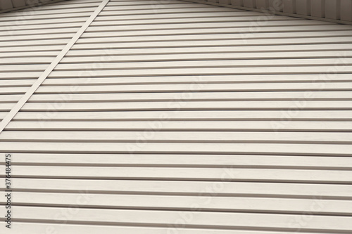 Striped plastic siding surface and piece of cornice. Construction and renovation of buildings. Light brown or beige background or wallpaper. Building materials and technologies