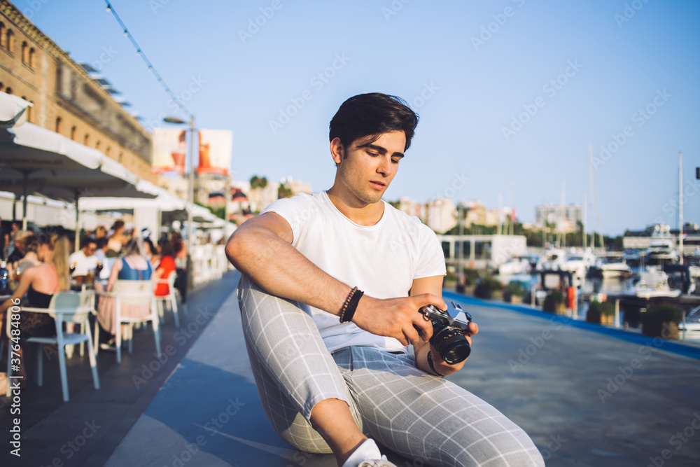 Young man with photo camera resting on street promenade