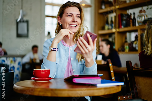 Happy young woman listening to voice message on smartphone in cafeteria