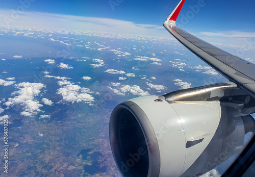 Airplane passenger window view of wing in flight with clouds on blue sky background.