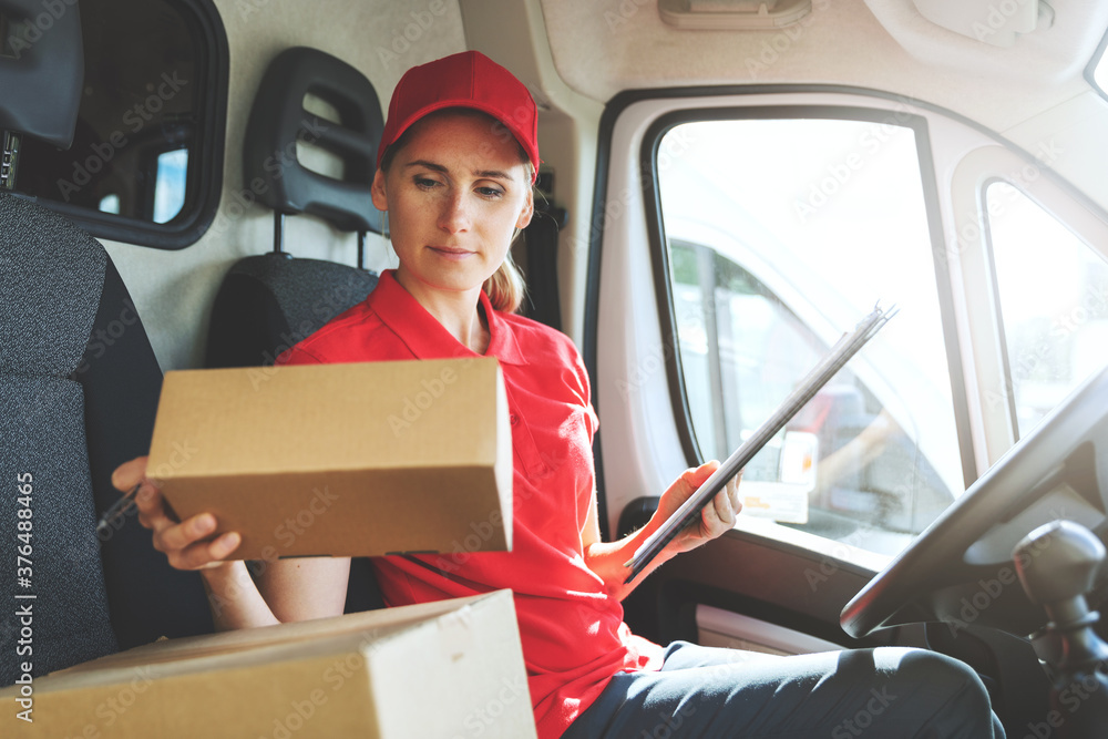 female delivery service worker in red uniform sitting in van and working with packages female delivery service worker in red uniform sitting in van and working with packages