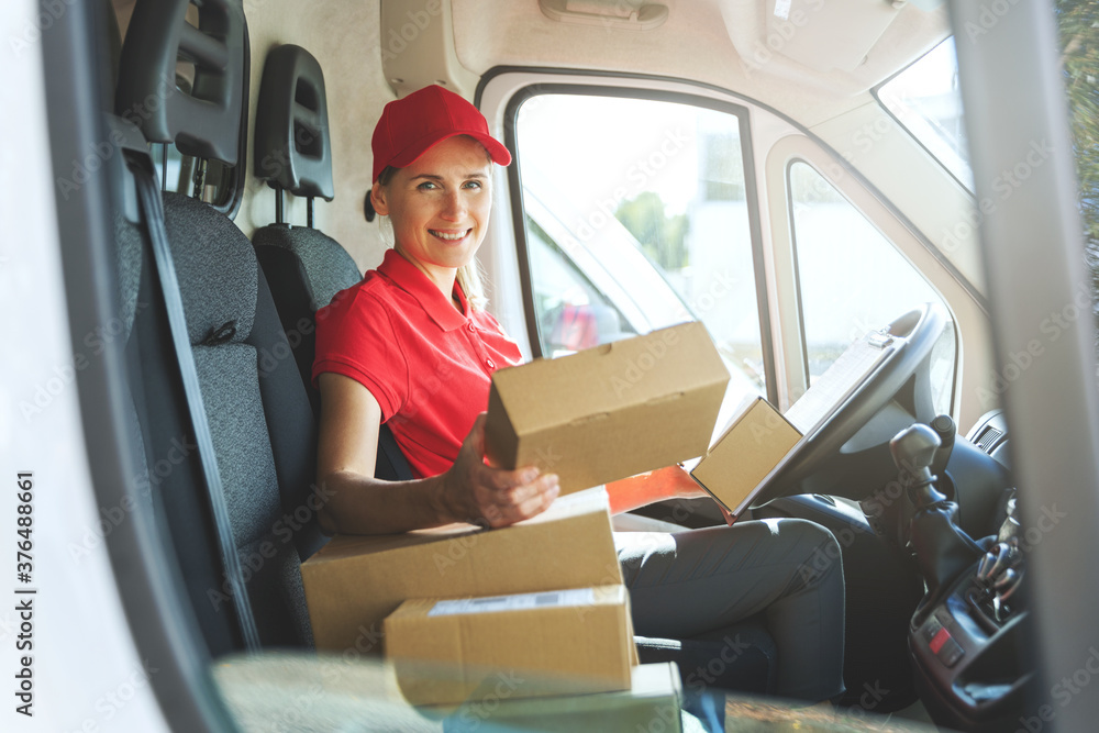 female delivery service worker in red uniform sitting in van with boxes. smiling at camera female delivery service worker in red uniform sitting in van with boxes. smiling at camera