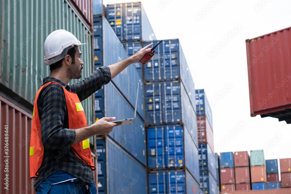 Engineer worker or technical standing and point out in the container yard shipping area and used radio communication to control loading containers into the stack. Industrial and import-export concept Engineer worker or technical standing and point out in the container yard shipping area and used radio communication to control loading containers into the stack. Industrial and import-export concept