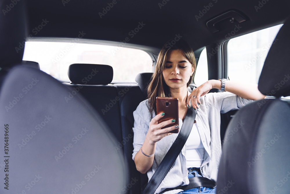 Focused young lady reading message on smartphone in car