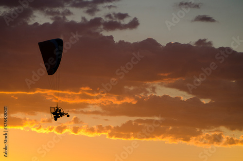 Silhouette of an ultralight flying at sunset in a cloudy sky