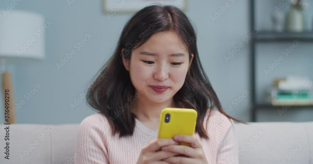 Portrait of pretty Asian girl sitting on couch and using smartphone in living room. Happy young woman chatting with friends, family, boyfriend and laughing. Social media, gadgets. Portrait of pretty Asian girl sitting on couch and using smartphone in living room. Happy young woman chatting with friends, family, boyfriend and laughing. Social media, gadgets.