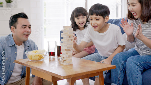 Asian family playing board game with wooden tower together at home. Son is pulls out a brick while sister, father and mother is looking and cheering.Weekend activity with entertainment at home concept