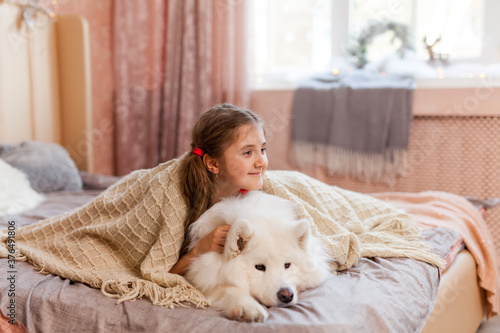 Smiling cute little girl hugging big white fluffy Samoyed dog at home © Inna Vlasova