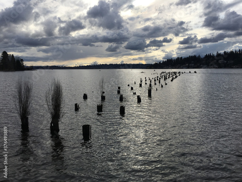 lake in winter

Serene lake view at dusk.  Stormy clouds and the last rays of the day reflected in the water.  Birds standing on rows of remanence wooden pillars of an old pier picking from the water.