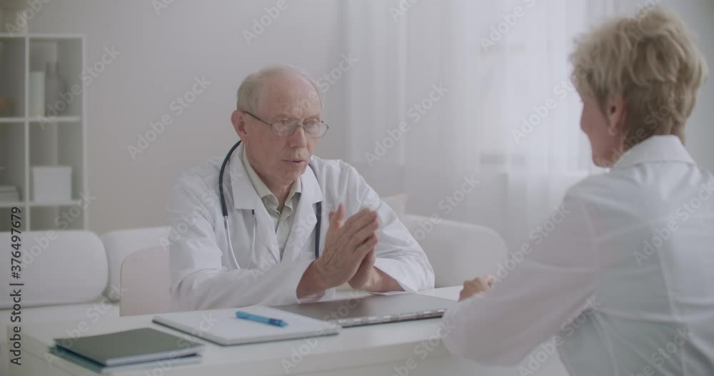 two physicians are talking in medical office in hospital, discussing sitting at table against each other, concilium two physicians are talking in medical office in hospital, discussing sitting at table against each other, concilium