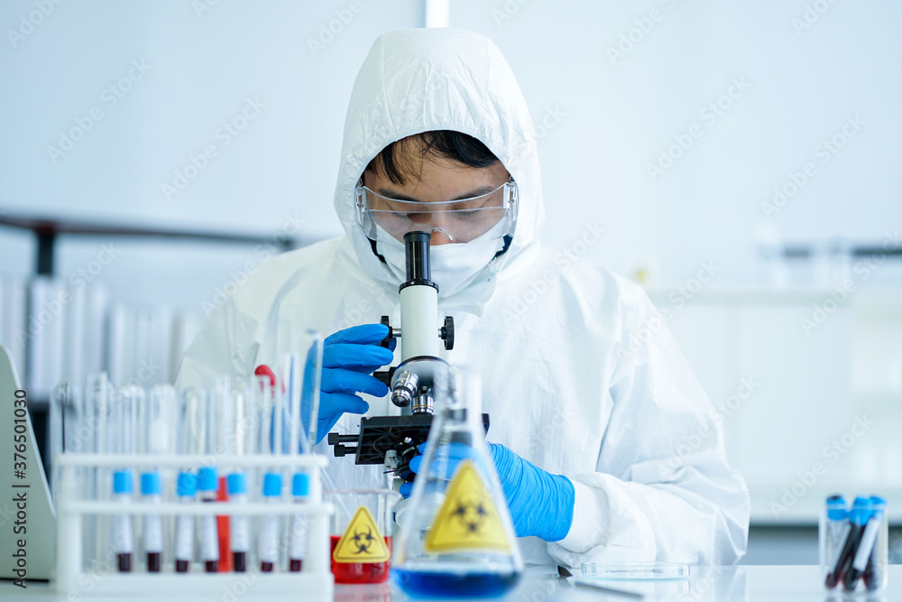 Asian medical scientist in protective white jumpsuit and glasses and face mask diagnosis virus with microscope in clinical laboratory Asian medical scientist in protective white jumpsuit and glasses and face mask diagnosis virus with microscope in clinical laboratory
