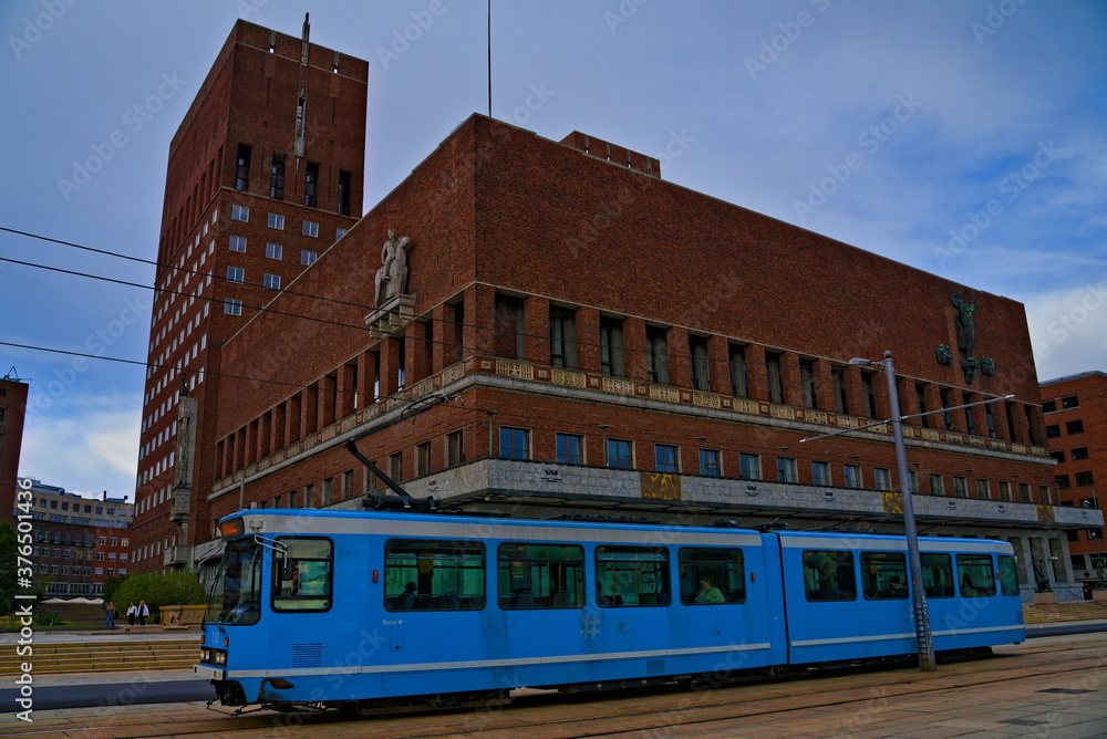 Oslo city hall, home of town administration for the municipality of Oslo with a blue city tram passing.