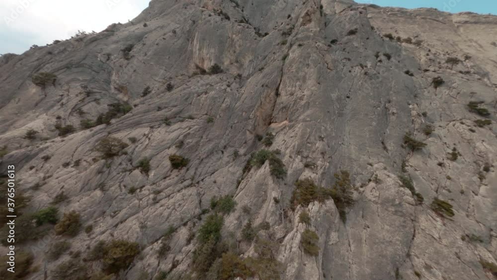Rocky mountain texture with flying fast FPV drone. High cliffs on blue sea shore dive view from above. Sport drone flying from top to bottom along rocky cliff on coast Rocky mountain texture with flying fast FPV drone. High cliffs on blue sea shore dive view from above. Sport drone flying from top to bottom along rocky cliff on coast