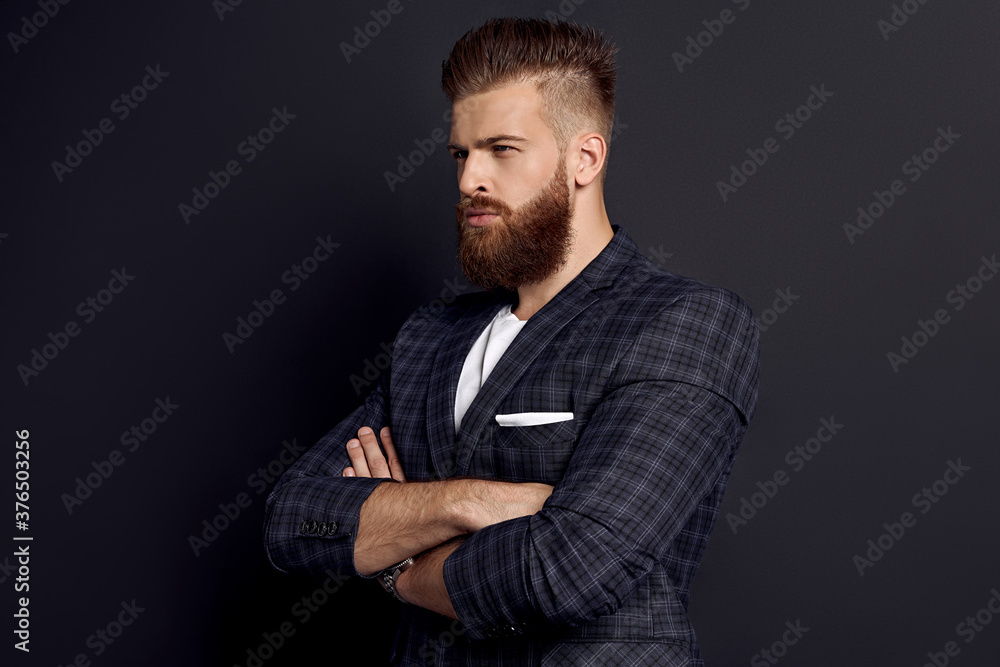 Handsome man keeping arms crossed while standing in profile against grey background