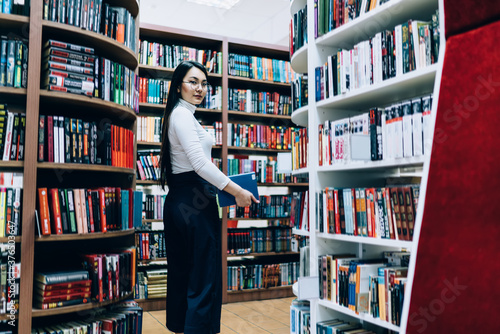 Asian female walking among bookshelves in library