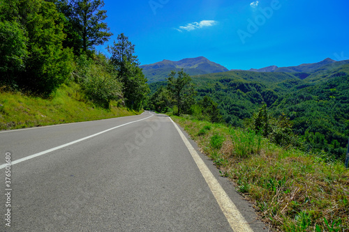 road to the mountains across green woods and blue sky. Copy space. Transportation, travel, tourism, camping, hiking concept. Success, movement concept 