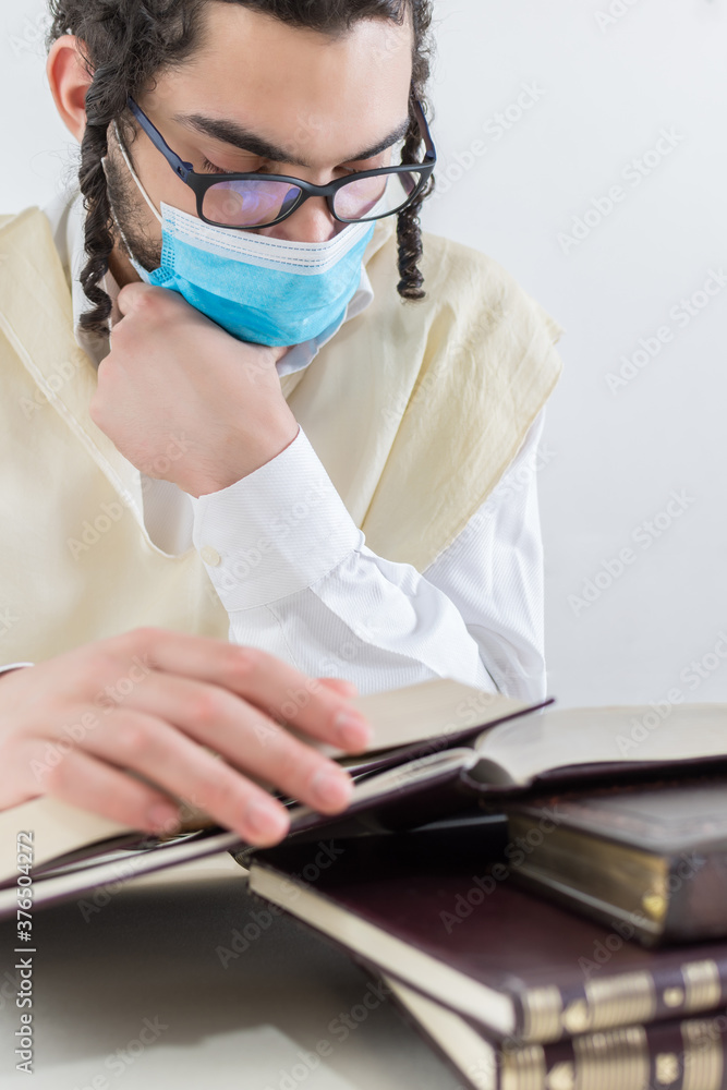 Young Orthodox Jew in a protective mask, studying religious texts. Covid-19. global pandemic Young Orthodox Jew in a protective mask, studying religious texts. Covid-19. global pandemic