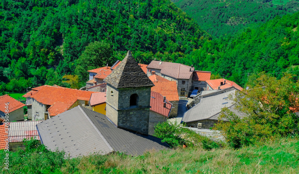 church in the village across green mountains close-up. Red, orange roofs. Scenery rural view. Background. Copy space. Italy, Emilia-Romagna, Cecciolo 