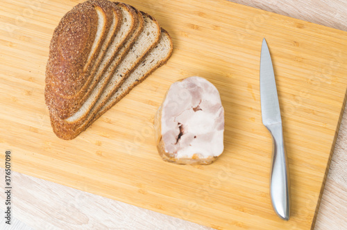 a whole piece of Turkey ham on the table, a knife, and bread for a sandwich without yeast