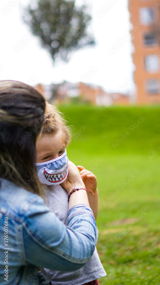 Caucasian mother putting face mask on her son in the park, Back to School
