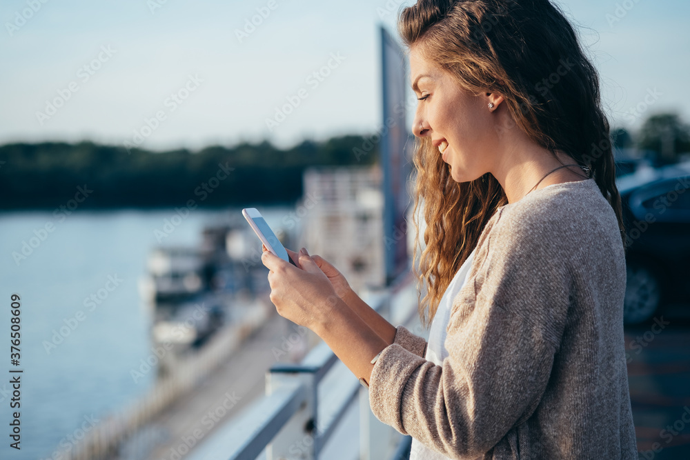 Naklejka premium Smiling young woman looking in mobile phone