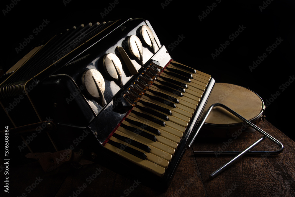 Old accordion, tambourine and triangle on rustic wooden surface with black background and Low