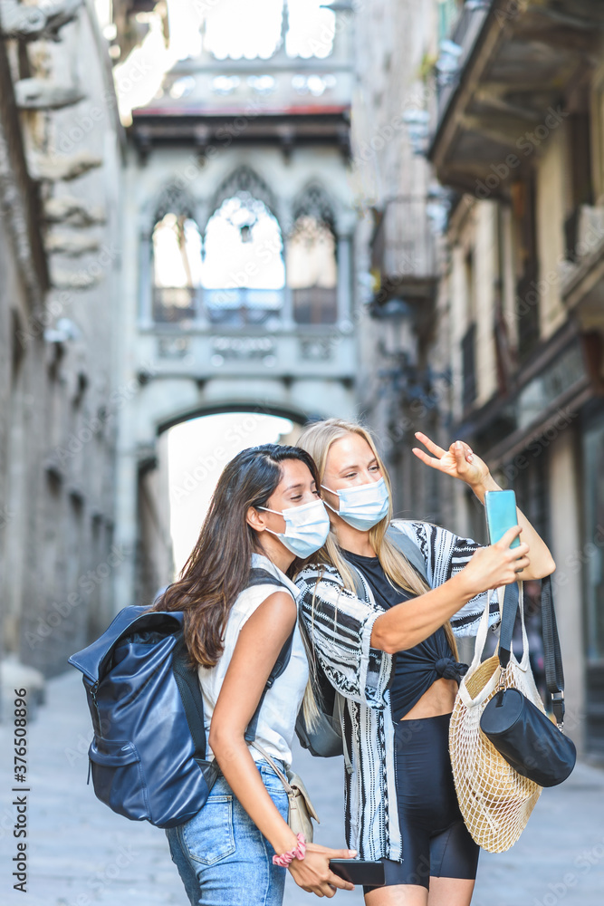 two beautiful female tourists taking selfie in the streets of Barcelona and doing gesture of victory