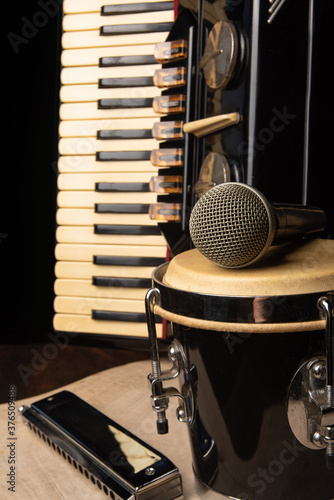 Old accordion, harmonica, bong and microphone on a rustic wooden surface with black background and low key lighting, selective focus.