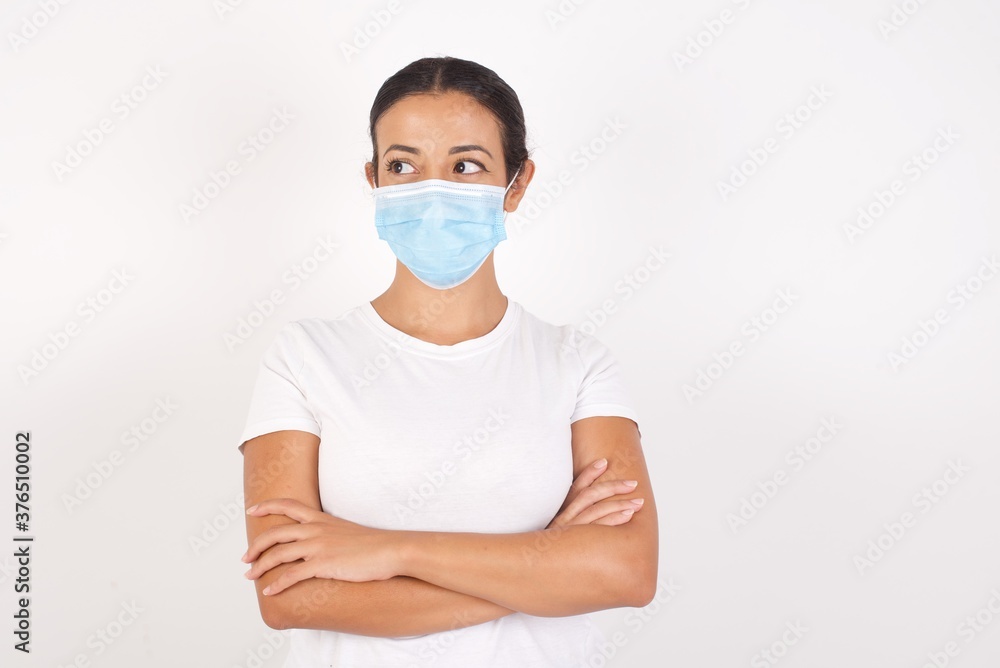 Dreamy rest relaxed Young arab woman wearing medical mask standing over isolated white background crossing arms, looks good Dreamy rest relaxed Young arab woman wearing medical mask standing over isolated white background crossing arms, looks good